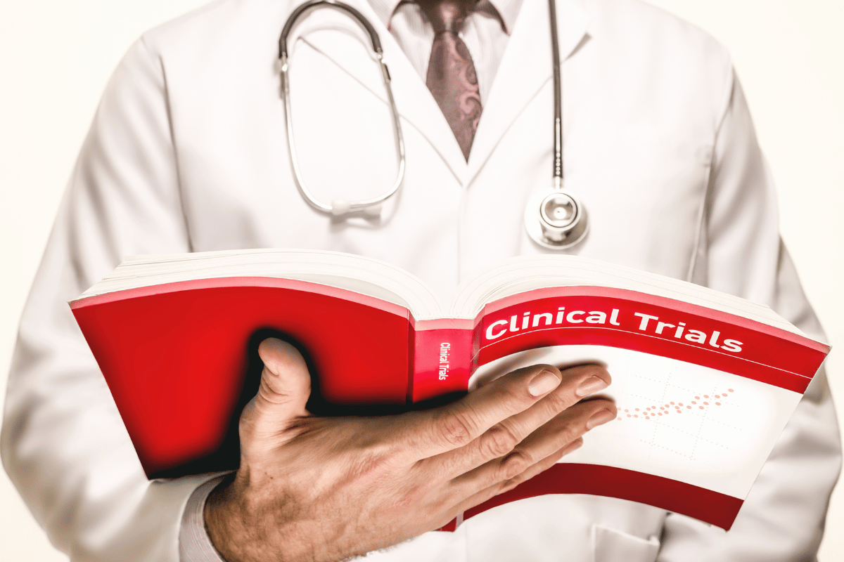Doctor holding and reading a red book titled 'Clinical Trials,' symbolising the risks involved in clinical trials.