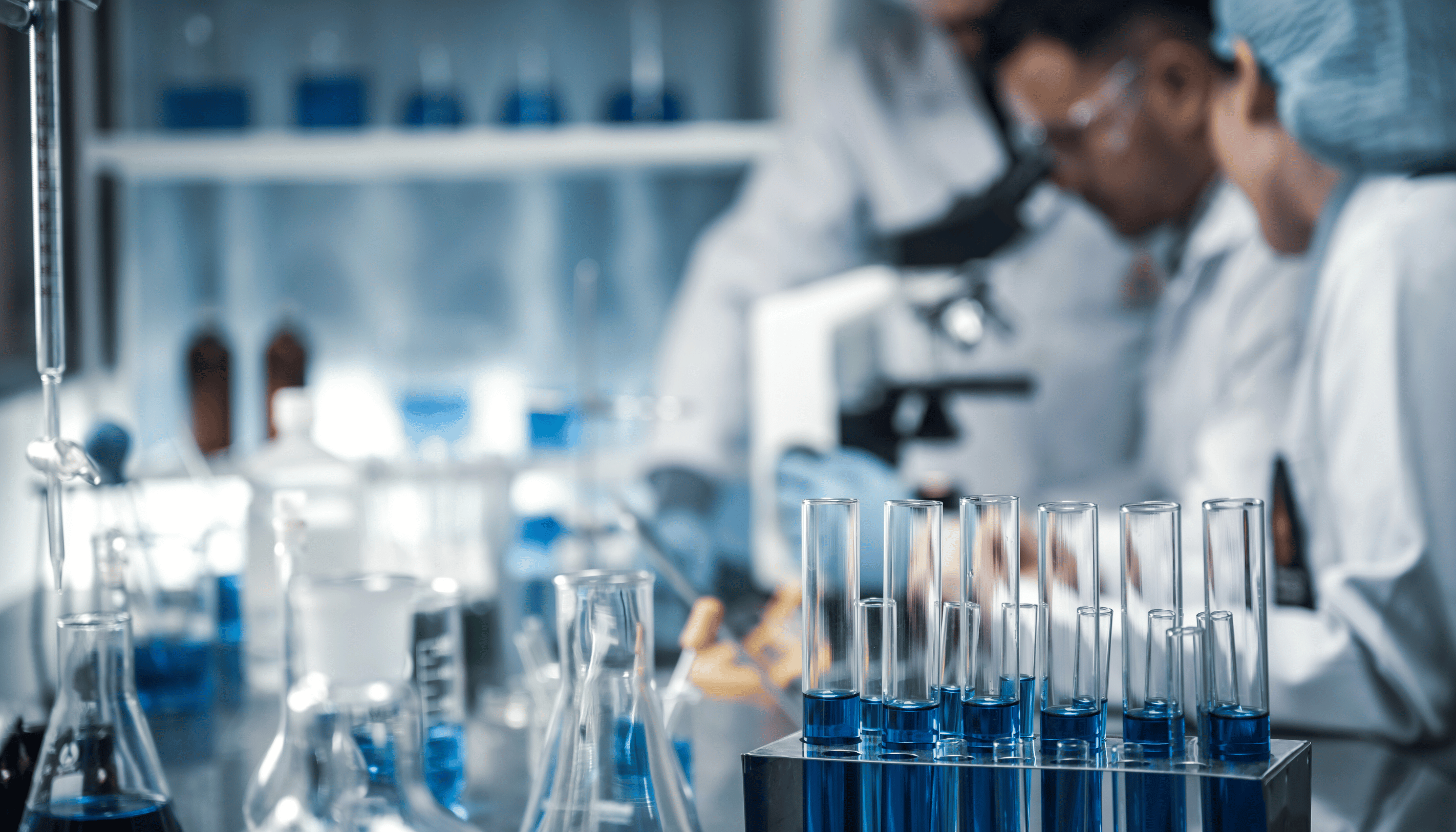 Laboratory scene with test tubes, beakers, and researchers using a microscope, representing medical research and clinical trials.